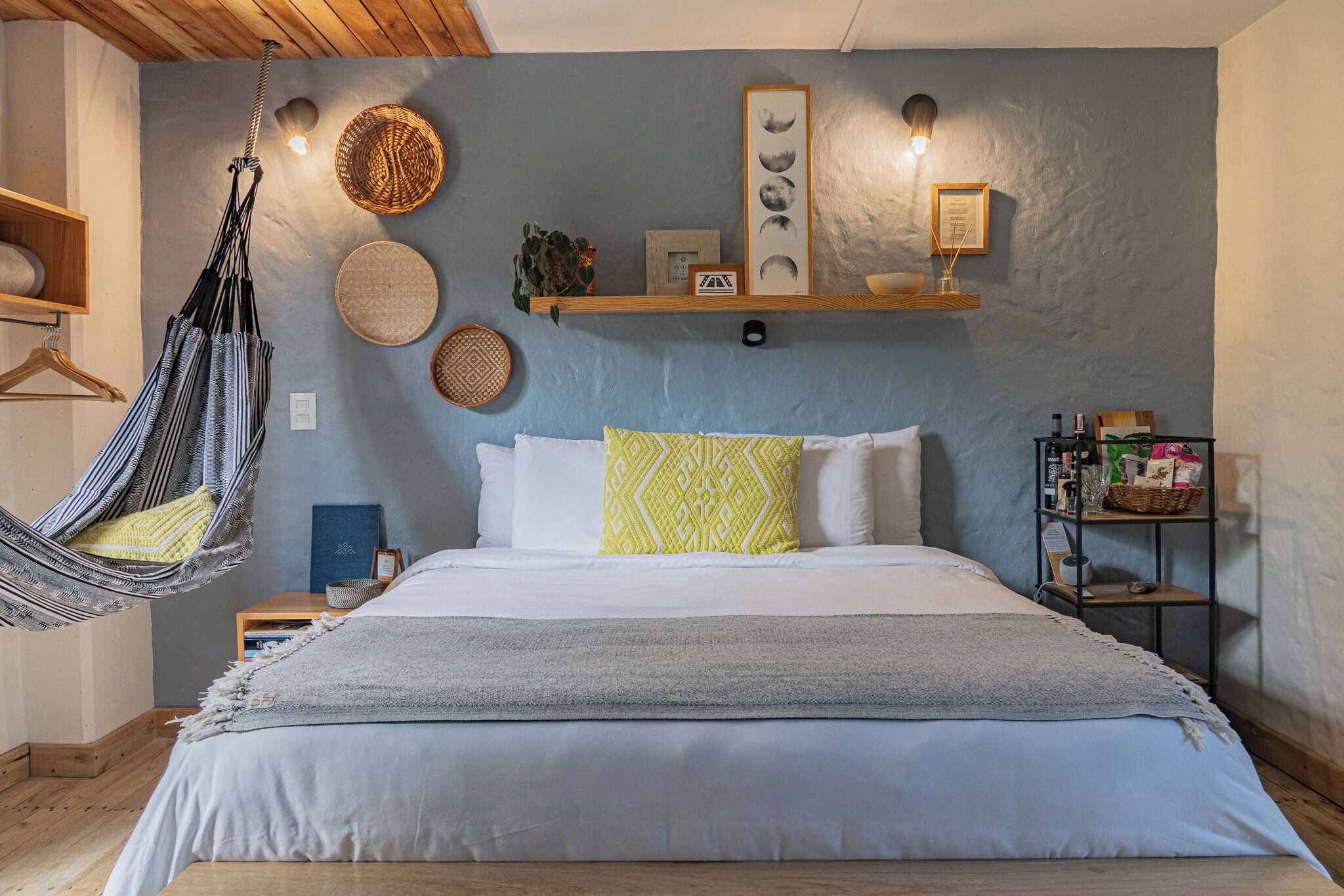 Un dormitorio con cama, una silla colgante, estante con objetos decorativos y una pared con calendario de fases lunares.