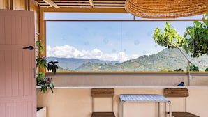 Un balcón con dos sillas de madera y una mesa de metal, una puerta de madera y vistas a montañas.