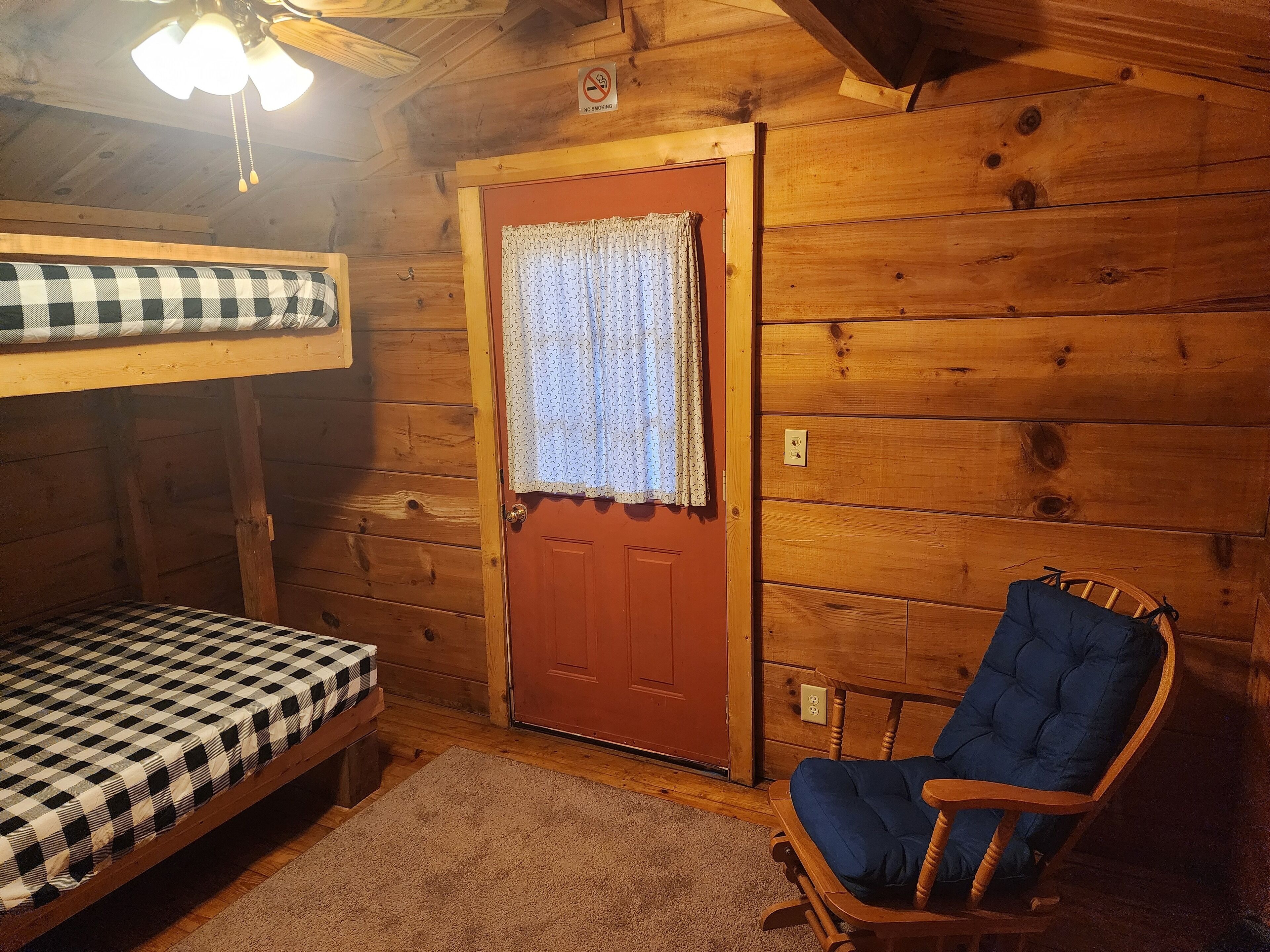 A wooden cabin room with a bunk bed, a rocking chair, and a door with a curtain.