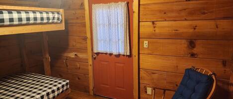 A wooden cabin room with a bunk bed, a rocking chair, and a door with a curtain.