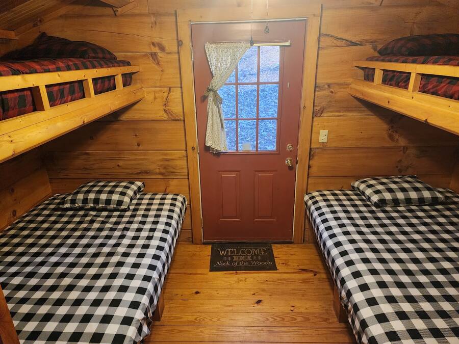 A cabin with two beds, each with a checkered bedspread, a wooden door, and a welcome mat.