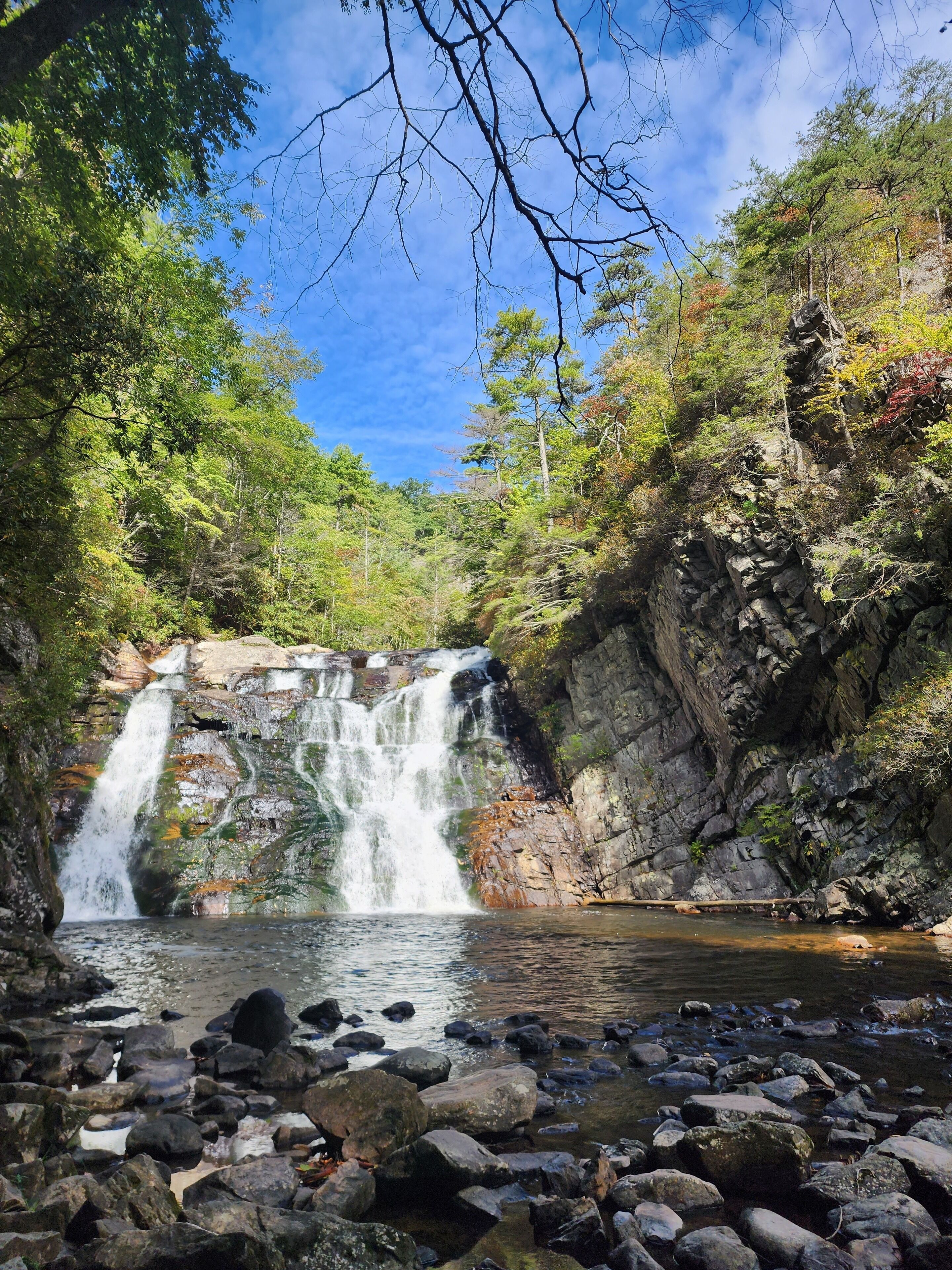 Ein Wasserfall, umgeben von felsigem Gelände und dichtem Grün.