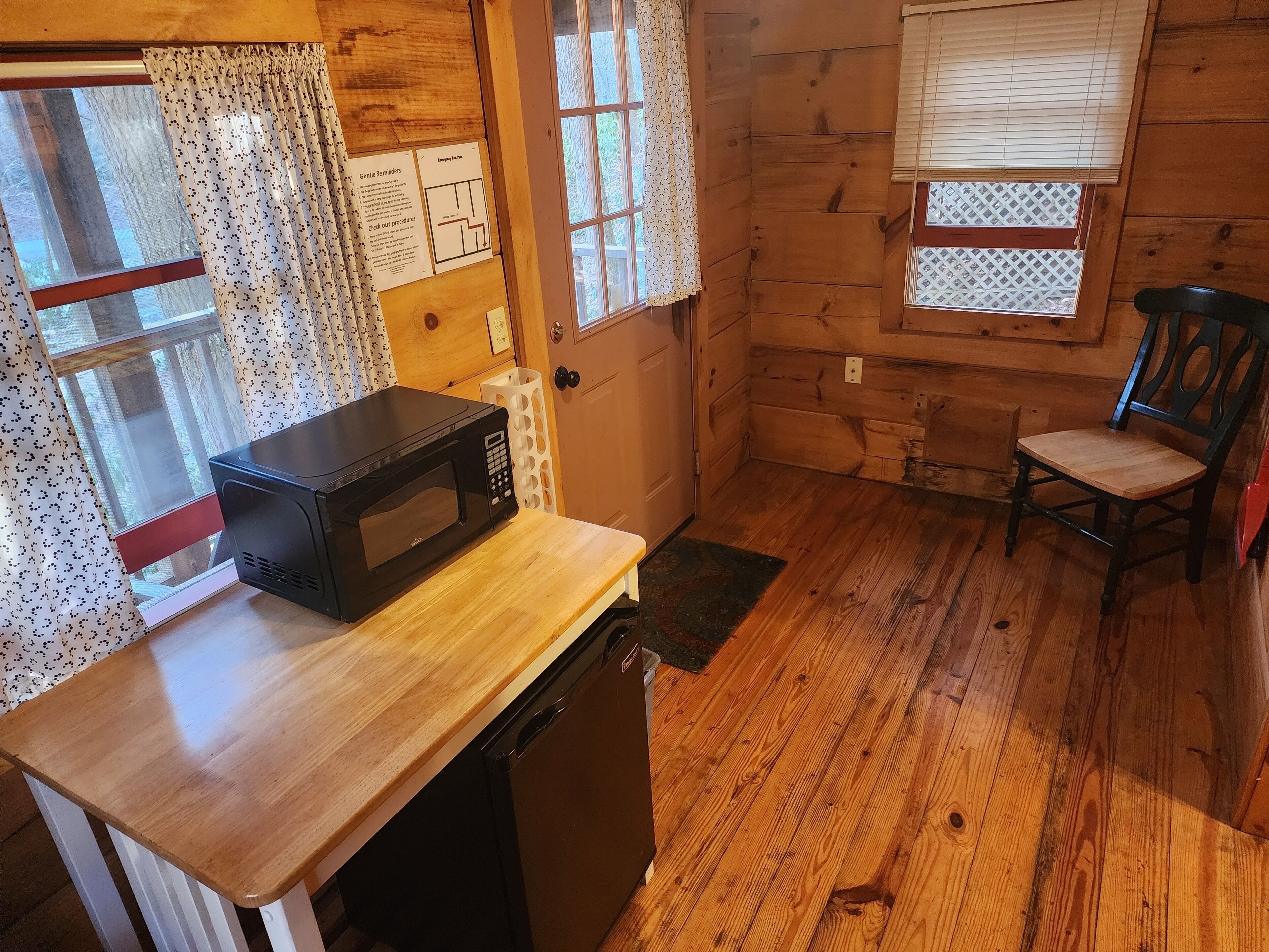 A compact kitchen with a microwave, dishwasher, wooden floor, and a chair.