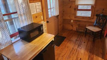 A compact kitchen with a microwave, dishwasher, wooden floor, and a chair.