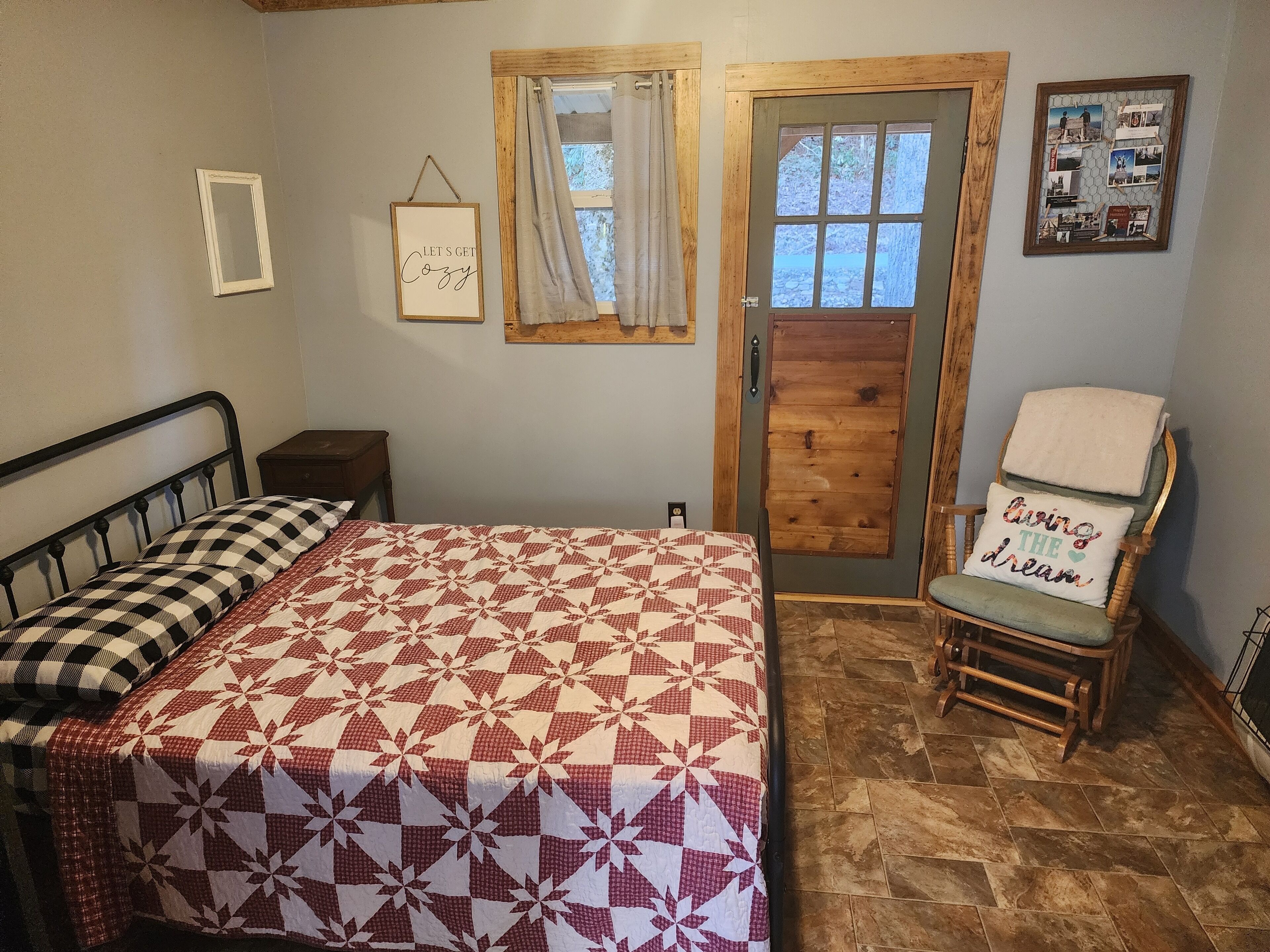 A cozy bedroom with a bed, a chair, a wooden door, and a wall with a picture frame and a sign.