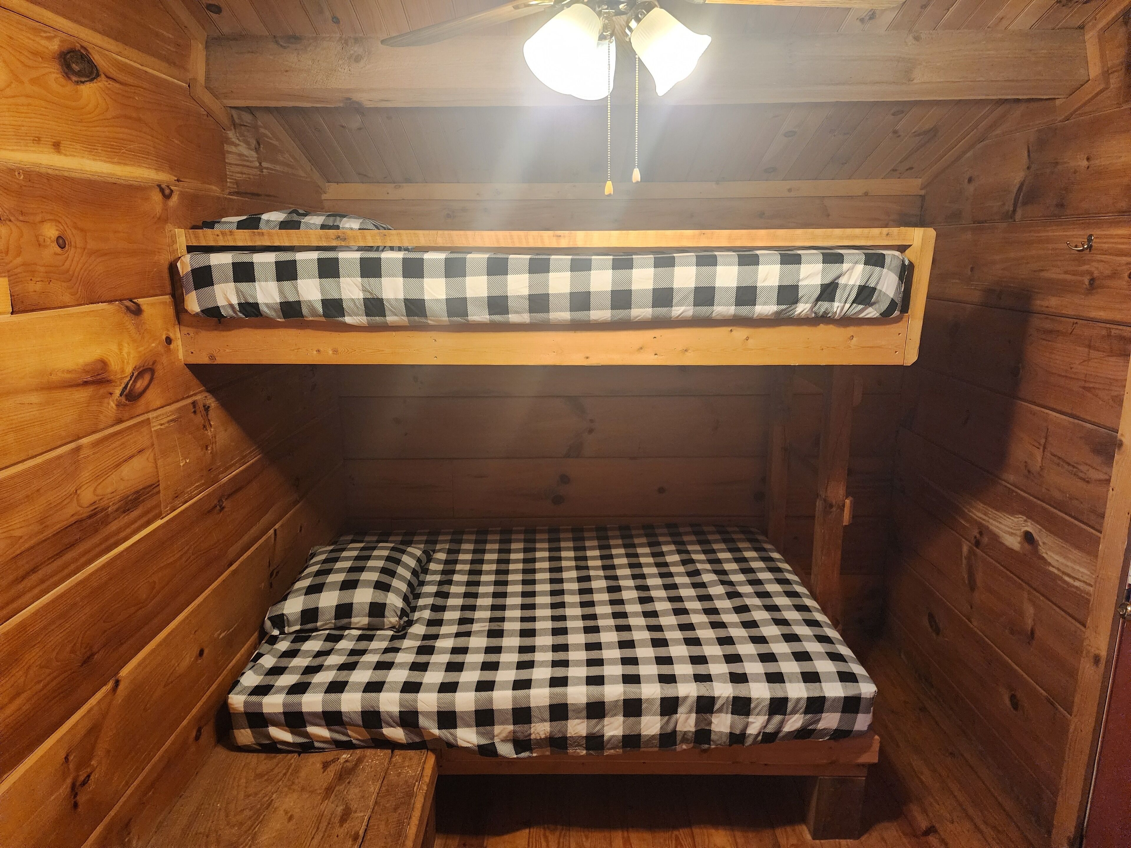 Un lit superposé avec une literie à carreaux dans une chambre de cabane en bois.