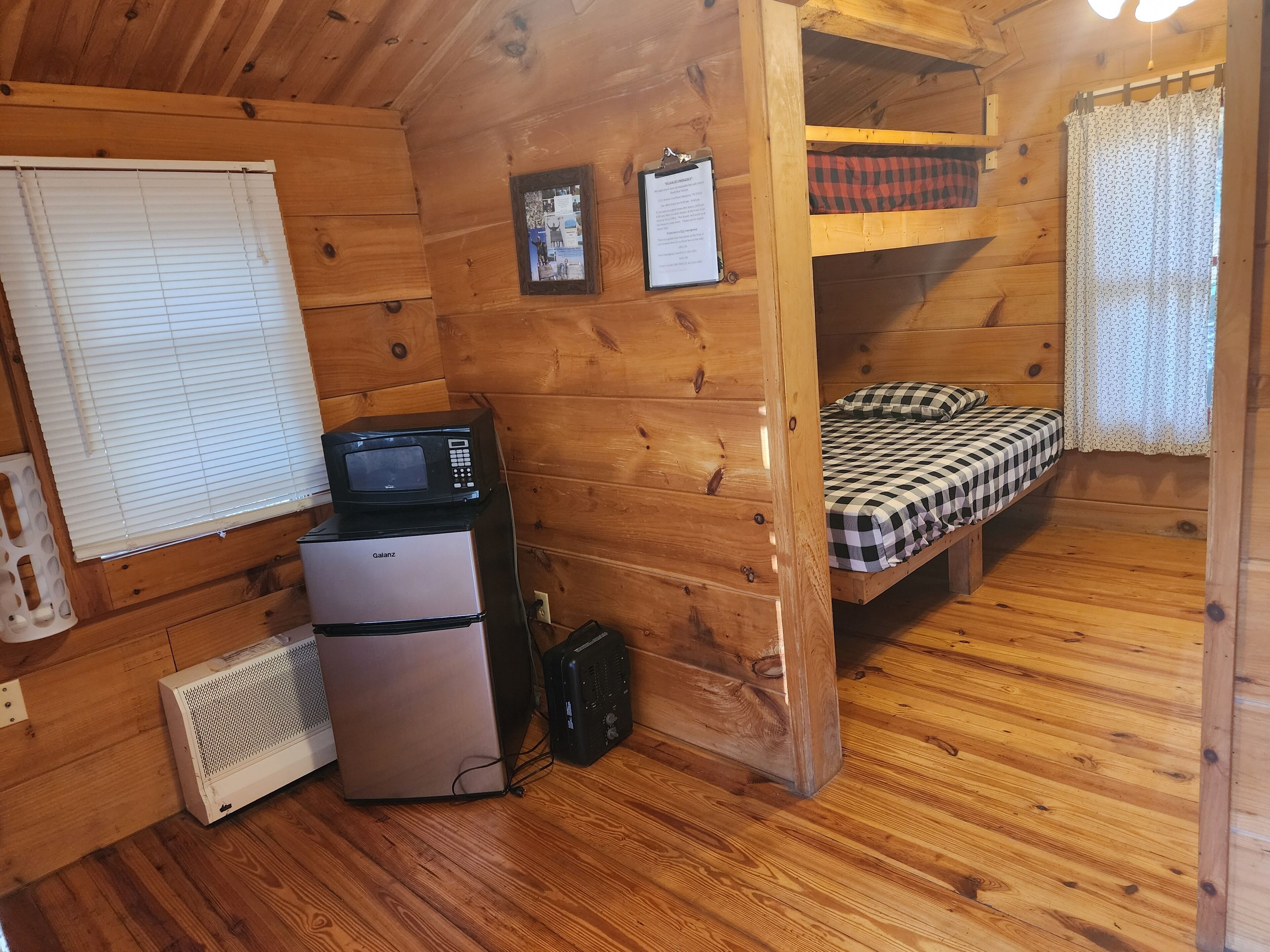 Een compacte houten kamer met een stapelbed, een koelkast, een magnetron en een kleine verwarming.