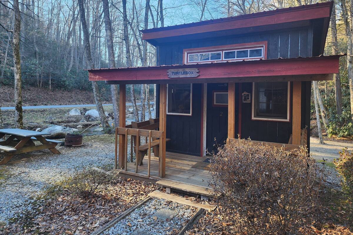 A rustic cabin named "Turtlebox" with a wooden deck, a small porch, and a view of the surrounding forest.