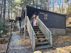 Una cabaña rústica con escaleras de madera que conducen a una puerta, rodeada de un bosque.
