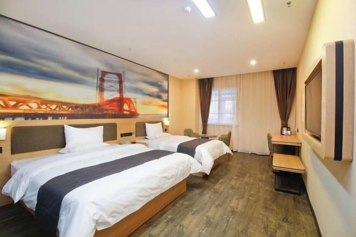 A hotel room with two beds, a desk, a chair, a TV, and a painting of a bridge.