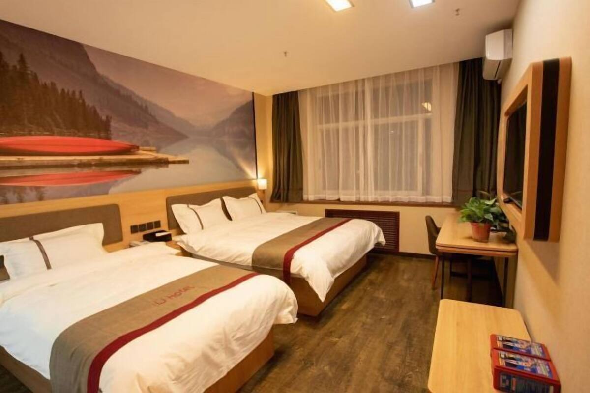 A hotel room with two beds, a desk, a window with curtains, and a painting on the wall.