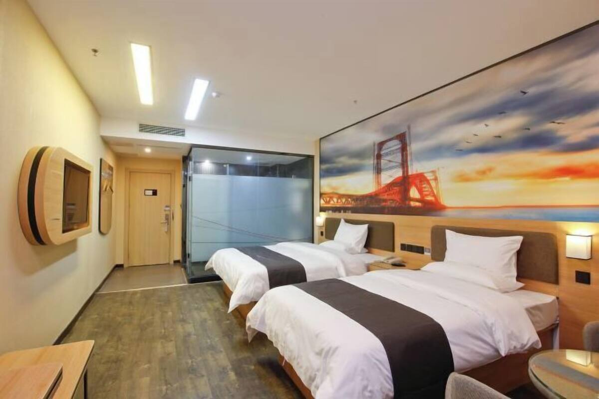 A hotel room with two beds, a desk, a chair, and a painting of a bridge.