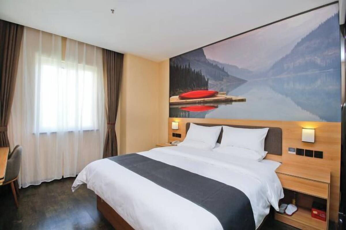 A hotel room with a large bed, a desk, and a painting of a lake and mountains on the wall.