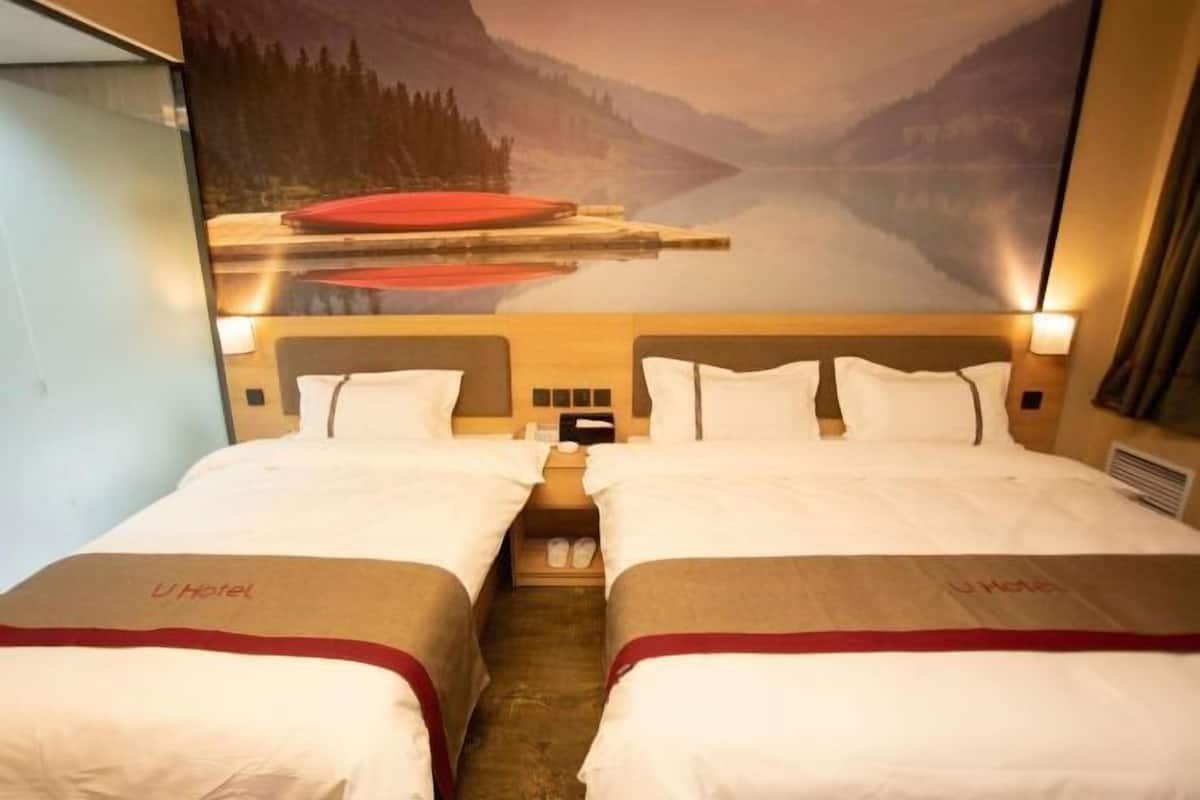 A hotel room with two beds, a nightstand, and a large window with a view of a lake and mountains.