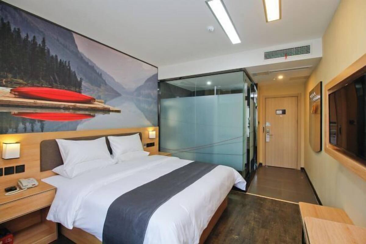 A hotel room with a bed, bedside table, and a large painting of a mountain landscape.