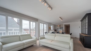 A spacious living area with a large window, a sofa, and a kitchen in the background. - Apartment in Knokke Near Lippenslaan (Knokke-Heist)