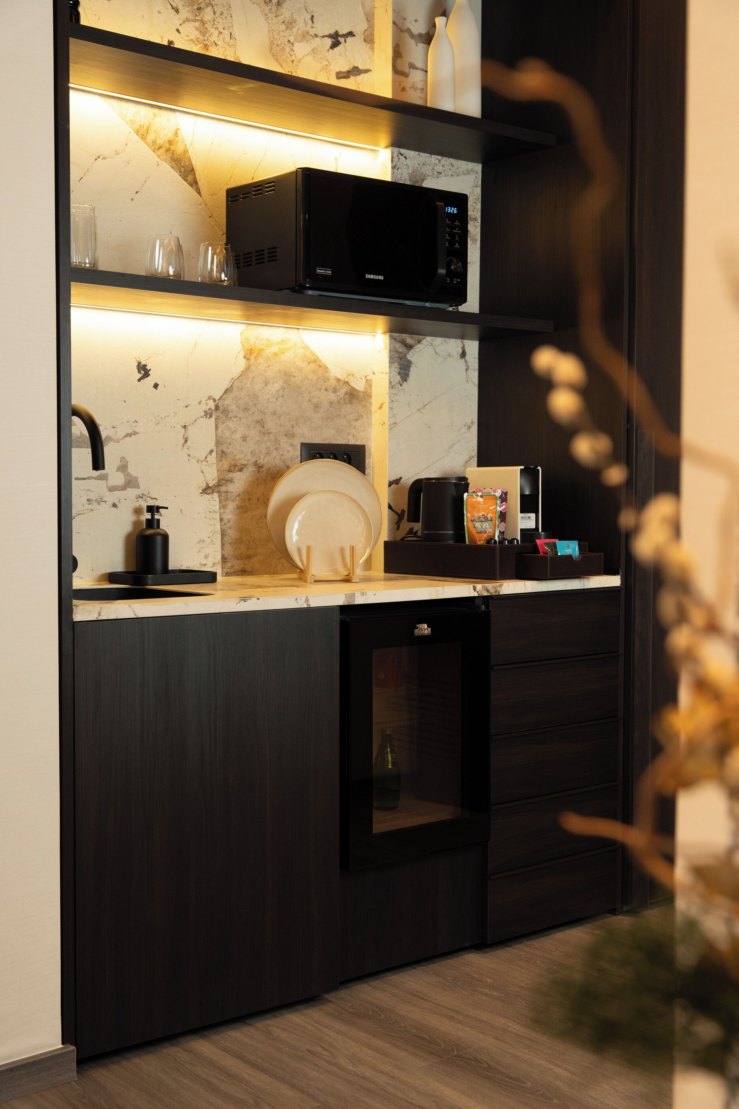 A modern kitchen with a built-in microwave, coffee maker, and a small refrigerator.
