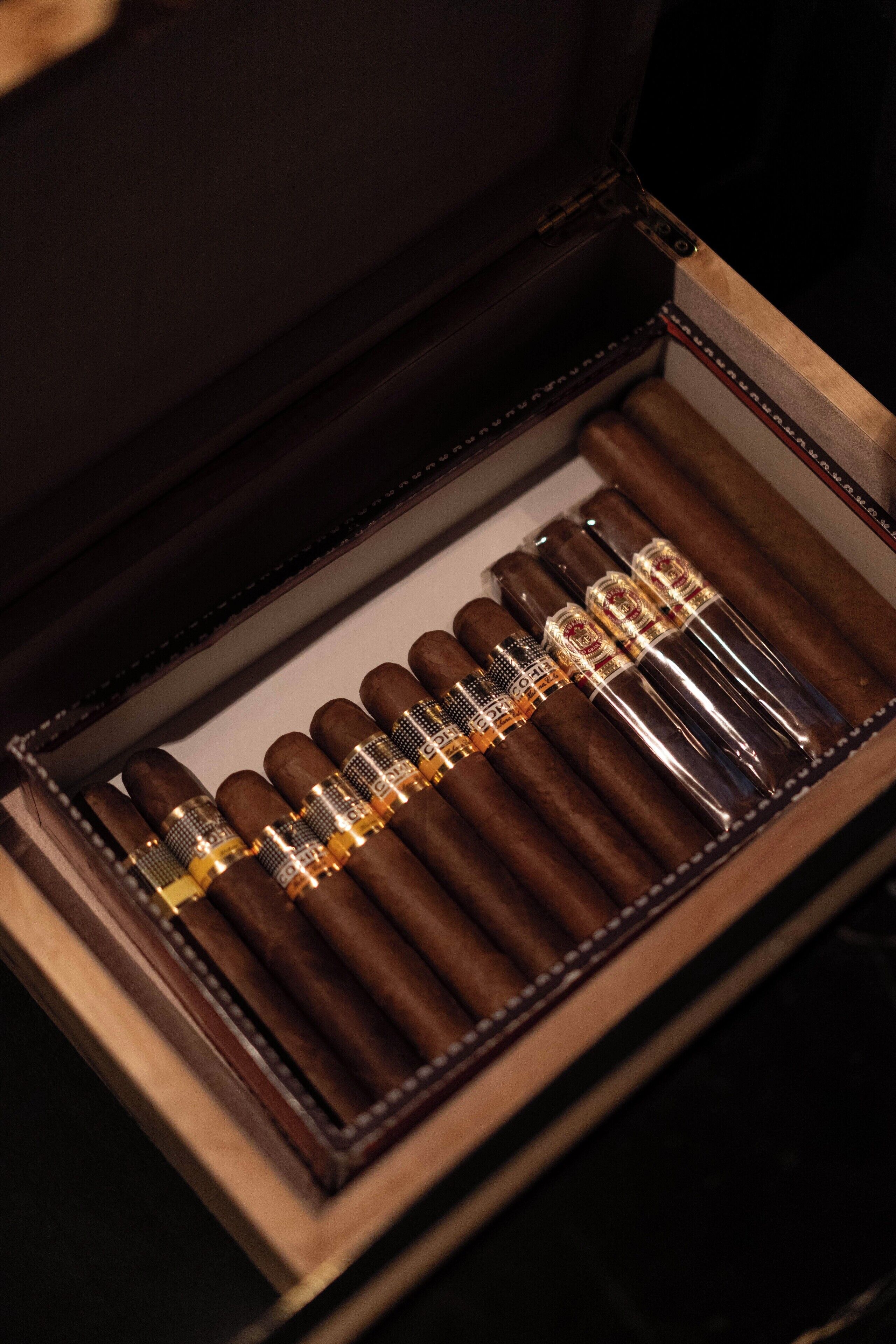 A wooden cigar box with a velvet interior, containing several cigars and a cigar cutter.
