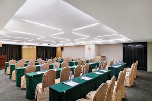 A conference room with rows of tables and chairs, a podium, and a projector screen.