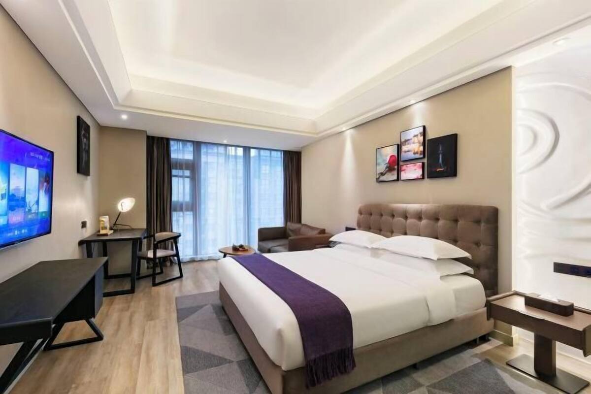 A hotel room with a large bed, a desk, a TV, and a window with curtains.