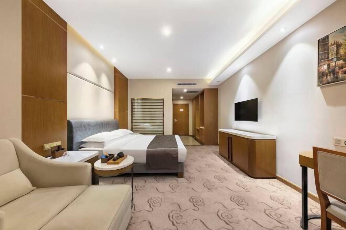 A hotel room with a bed, a sofa, a TV, a desk, and a bathroom with a shower and toilet.