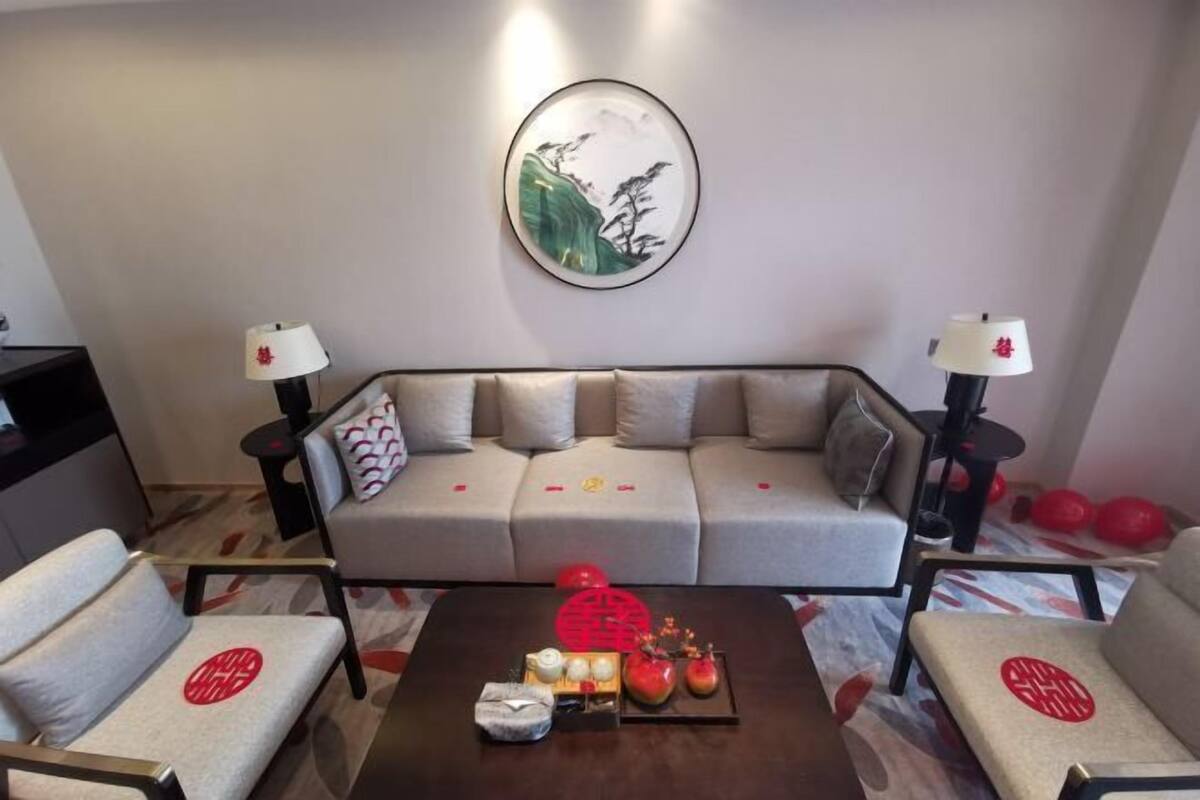 A modern living room with a sofa, two armchairs, a coffee table with decorative items, and wall-mounted lamps.
