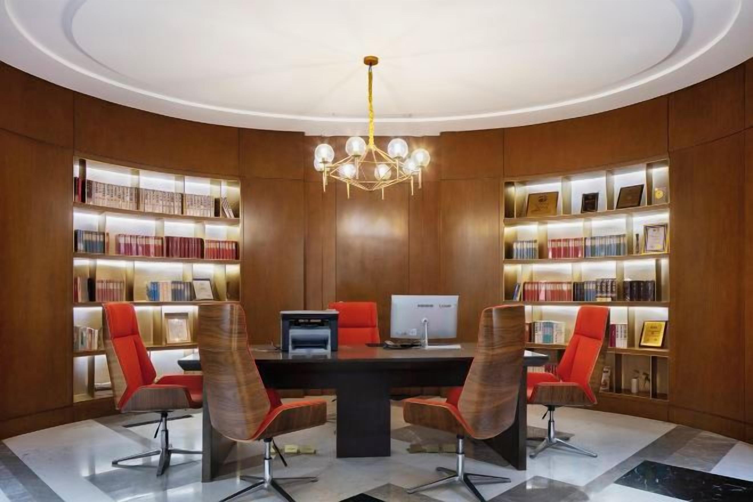 A library with a round table, bookshelves, and a chandelier.