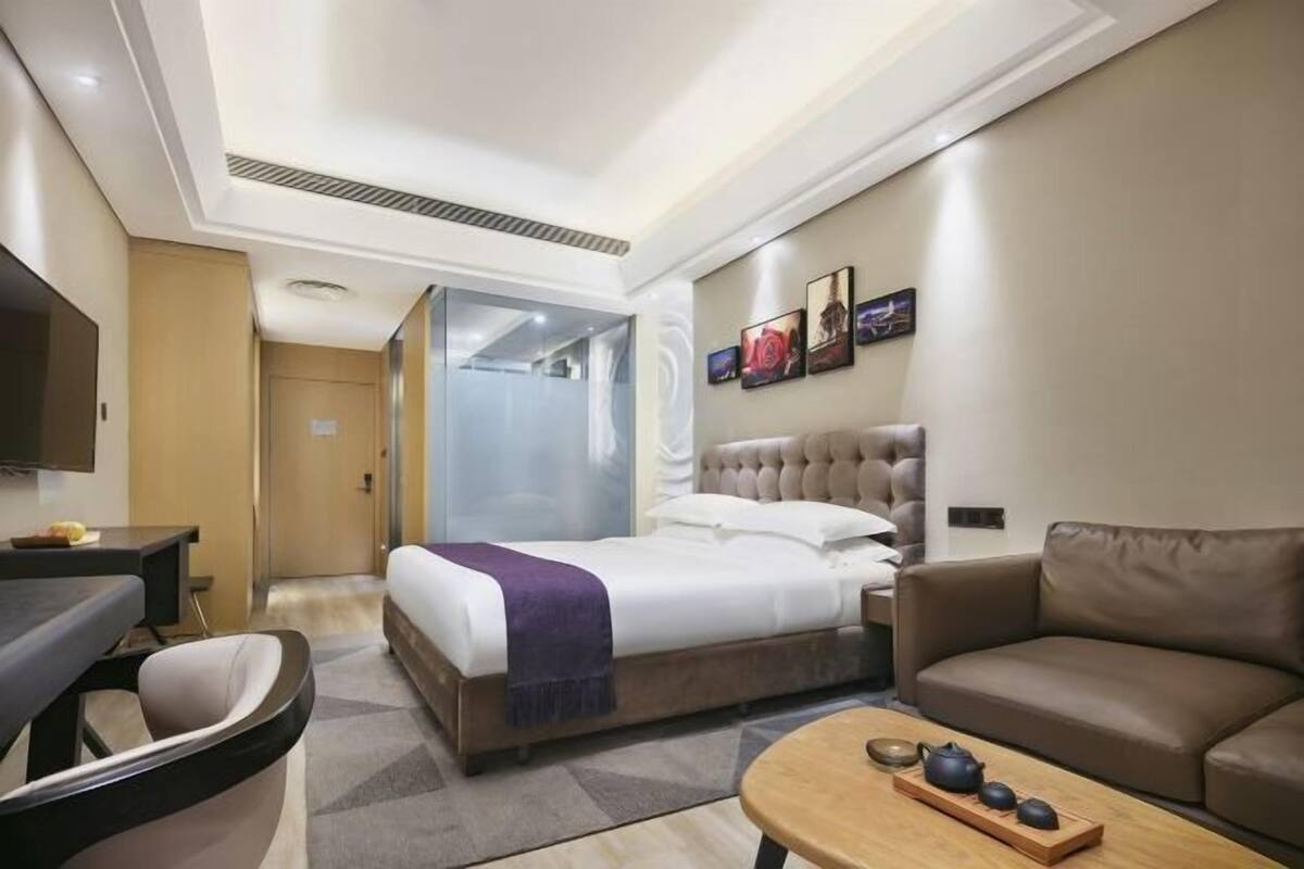 A hotel room with a bed, a sofa, a coffee table, a TV, and a desk.