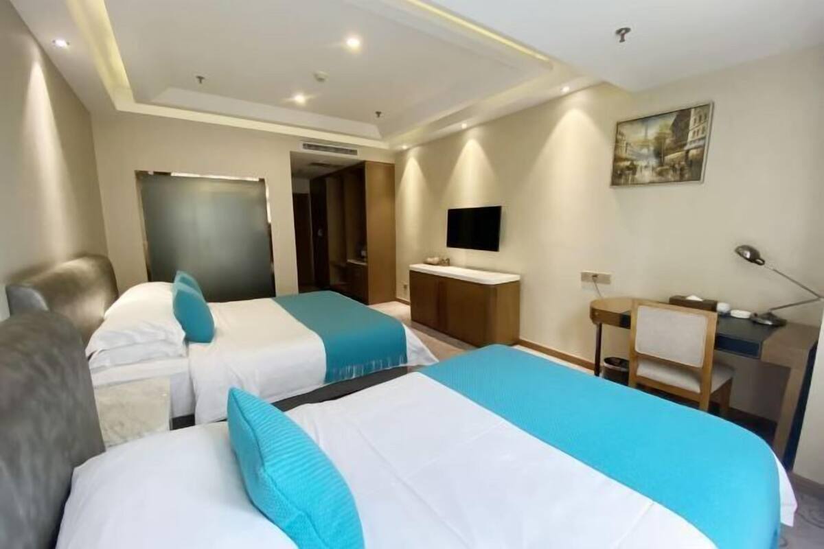 A hotel room with two beds, a desk, a chair, a TV, and a painting on the wall.