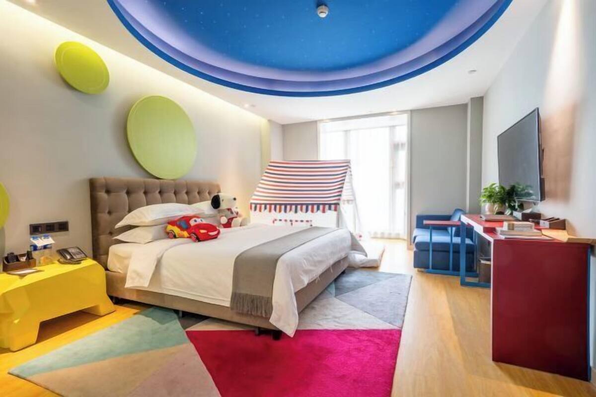 A modern bedroom with a tufted headboard, a striped canopy, a desk with a chair, and a large window.
