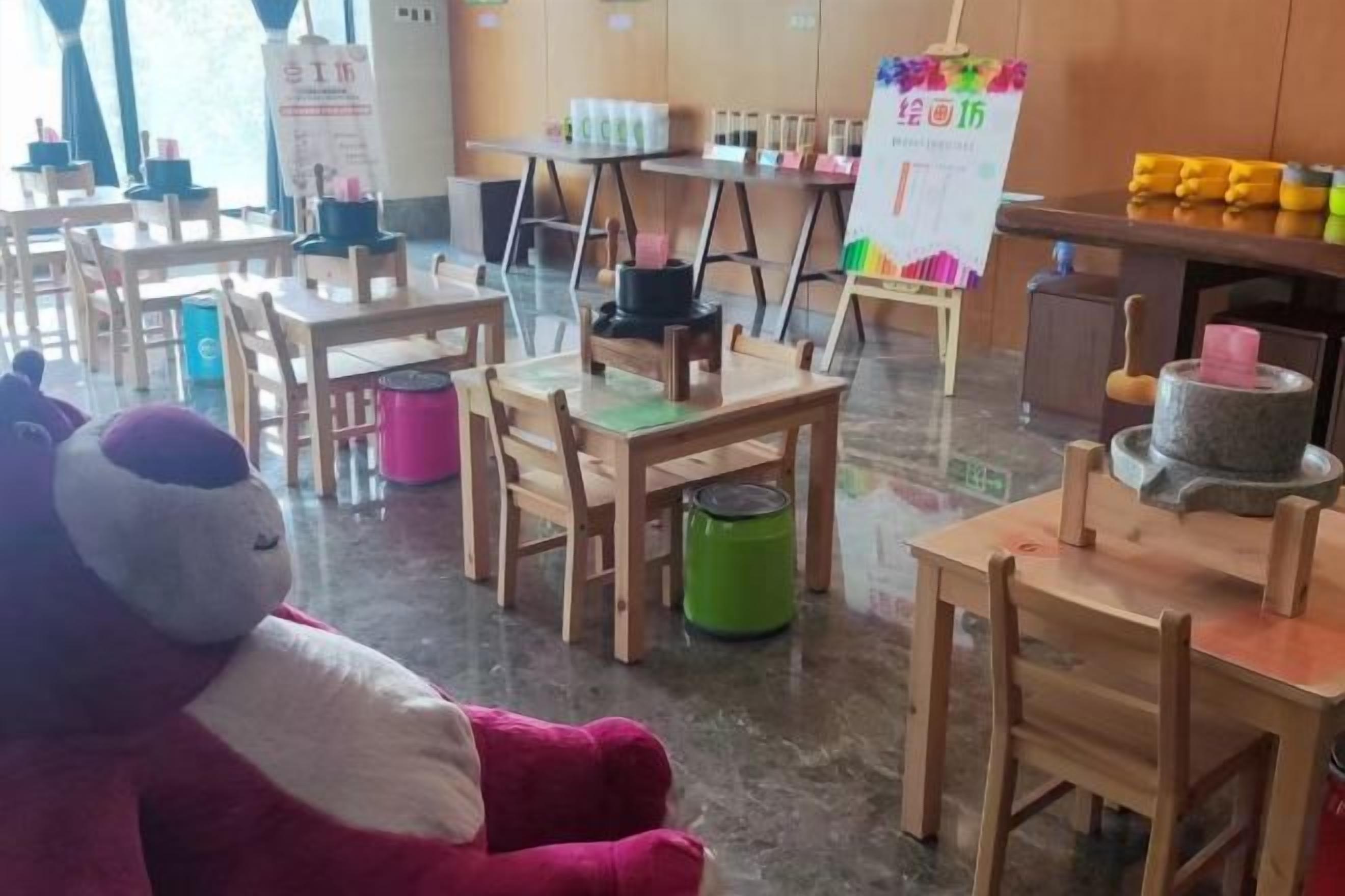 Une salle de classe avec des tables et des chaises en bois, un jouet en peluche et un tableau blanc.
