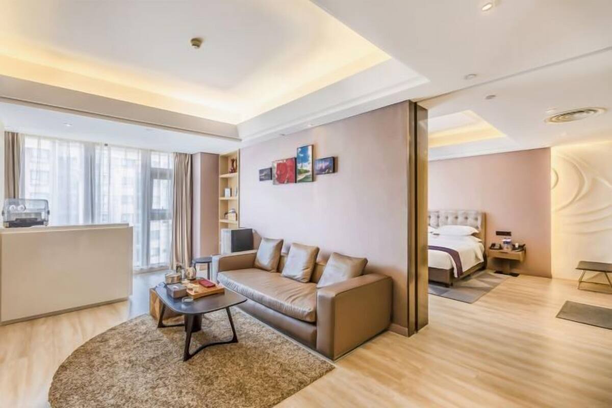 A modern hotel room with a sofa, a coffee table, a bed, and a desk.
