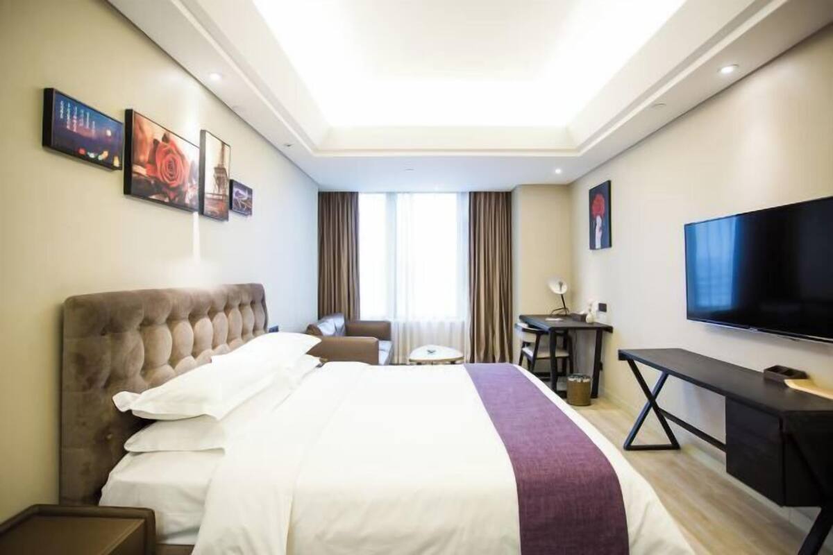 A hotel room with a large bed, a desk, a television, and artwork on the walls.