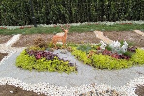 A garden with a deer statue, various plants, and a hedge in the background.