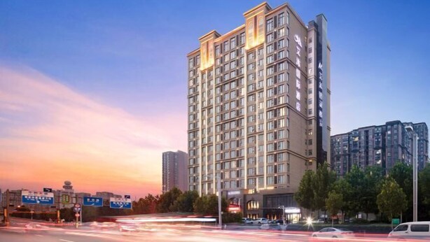 A multi-story hotel with a modern design, featuring a prominent entrance and a large parking area in front. - Zhengzhou Aimu International Hotel (Zhengzhou)