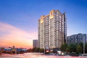 A multi-story hotel with a modern design, featuring a prominent entrance and a large parking area in front. - Zhengzhou Aimu International Hotel (Zhengzhou)