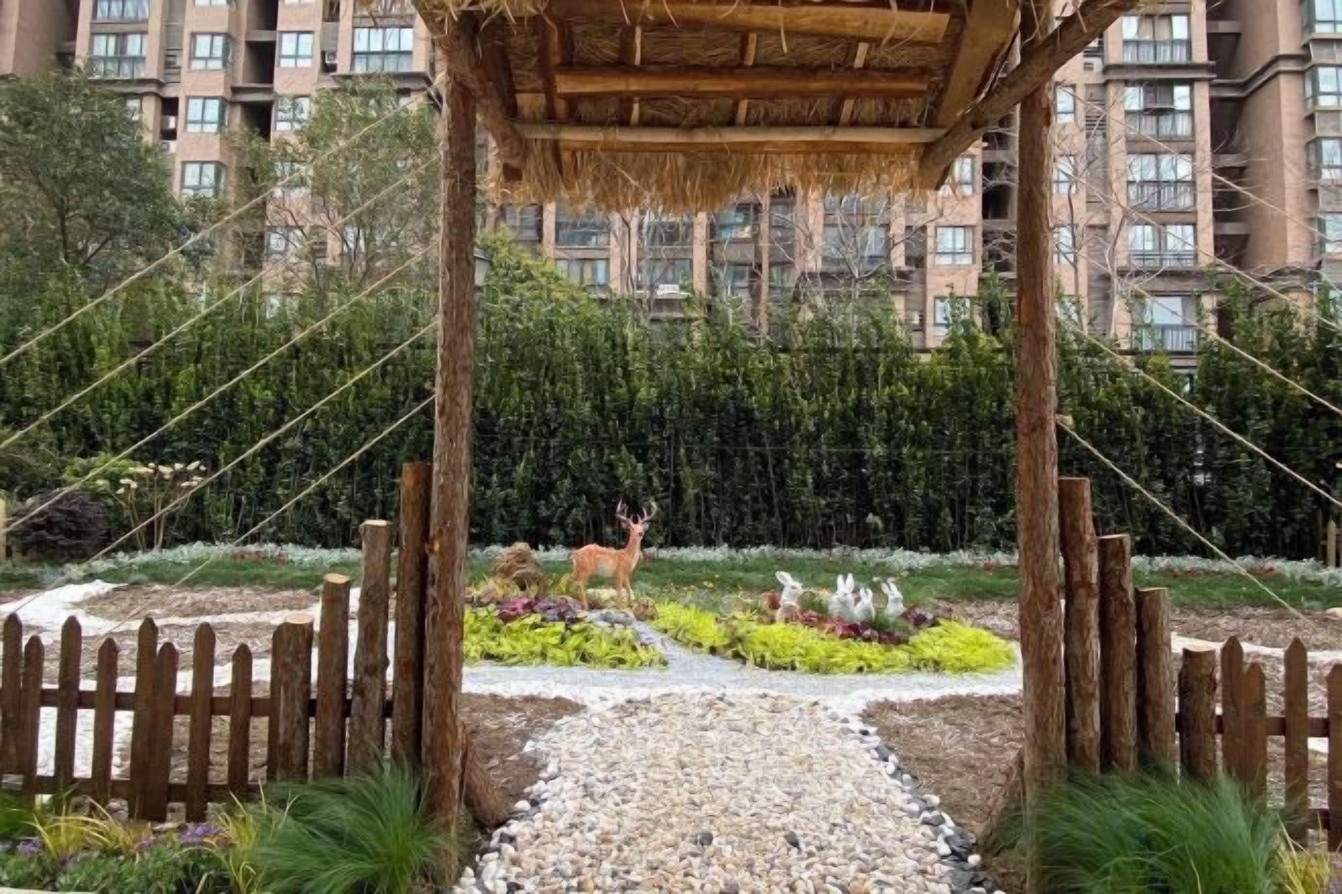 Un jardin agrémenté d’une pergola en bois, d’une statue de cerf et d’une zone délimitée par une clôture.