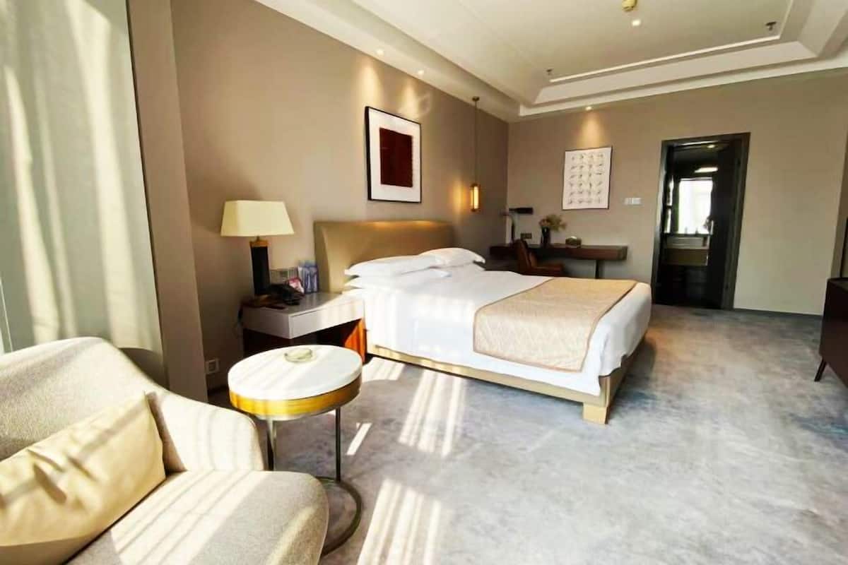A hotel room with a bed, a chair, a bedside table with a lamp, and a framed picture on the wall.
