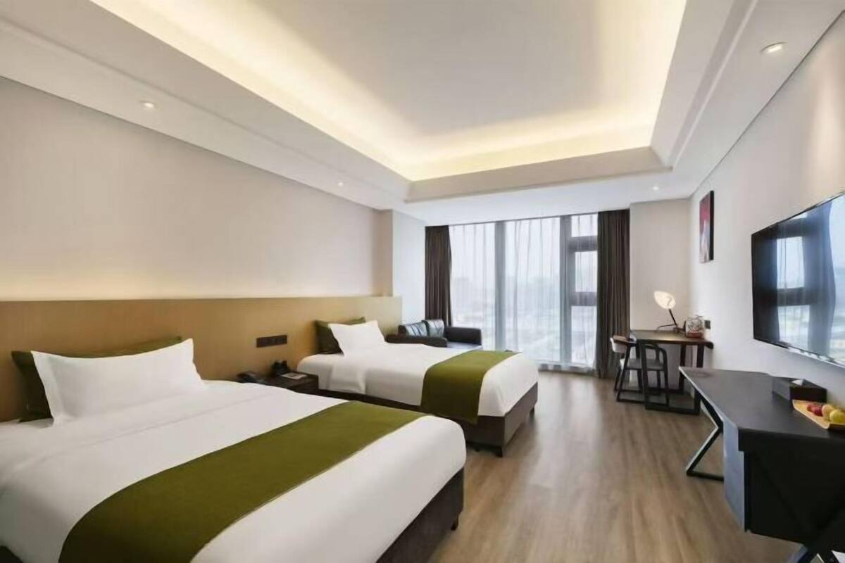 A hotel room with two beds, a desk, a chair, a TV, and a large window.