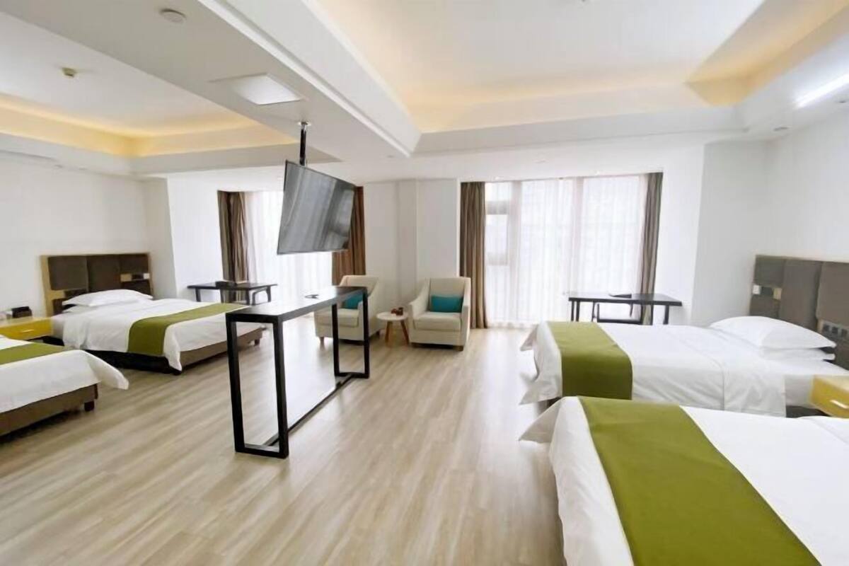 A hotel room with four beds, a TV, a desk, and a chair.