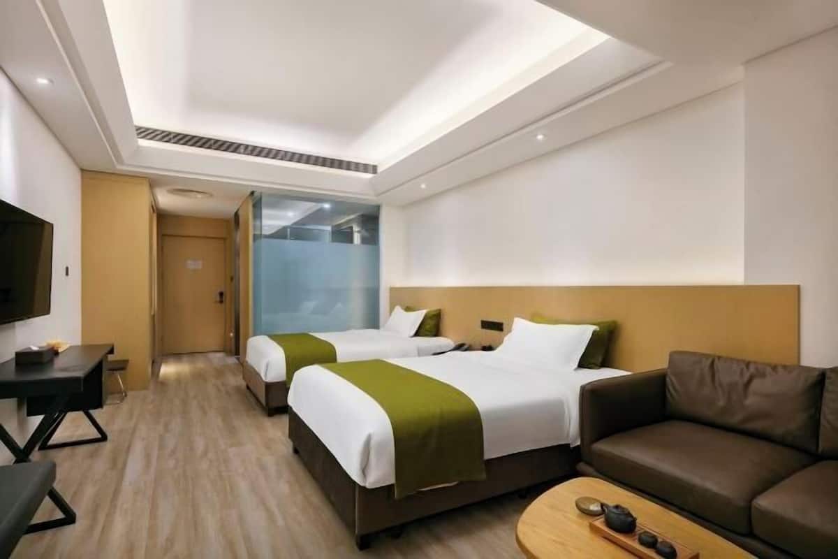 A hotel room with two beds, a sofa, a TV, and a wooden coffee table.