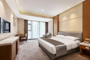 A hotel room with a large bed, a desk, a chair, a TV, and a window with curtains. - Zhengzhou Aimu International Hotel (Zhengzhou)