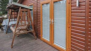 Una baita in legno con una veranda, un'altalena e due porte scorrevoli in vetro.