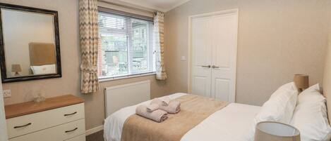 A bedroom with a bed, a dresser, a mirror, a window with curtains, a radiator, and a door.