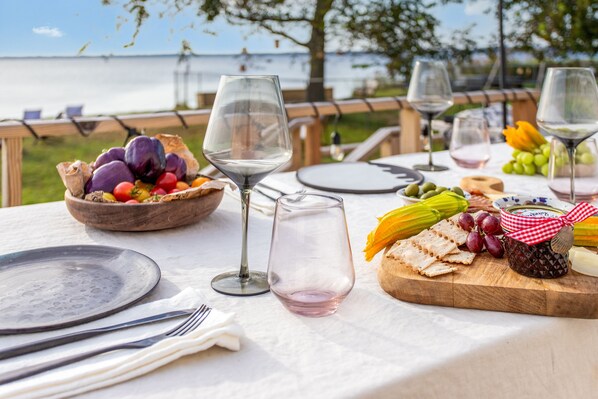 An outdoor dining setup with a table set for two, featuring a variety of fruits, cheeses, and crackers.
