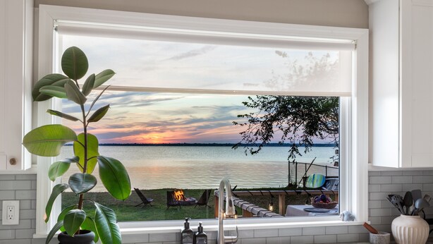 Una cocina con un ventanal grande que da a vistas de un lago, un lavamanos y una planta en maceta.