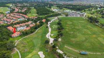 Vue aérienne d’un terrain de golf avec une zone résidentielle, un plan d’eau et un point de repère.