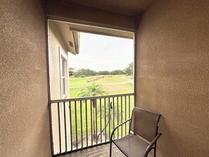 A balcony with a chair, a view of a grassy area, and a building in the background.