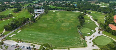 An aerial view of a golf course with multiple holes, a parking area, and surrounding greenery.