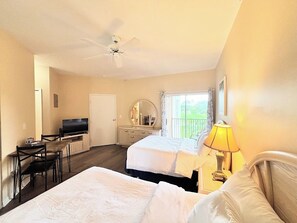 A hotel room with two beds, a desk with a TV, a dresser, and a balcony with a view.